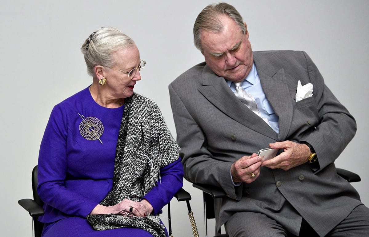 Tanskan kuningatar Margareeta II ja puoliso prinssi Henrik istuvat vierekkäin. Prinssi Henrikillä on älypuhelin kädessään.