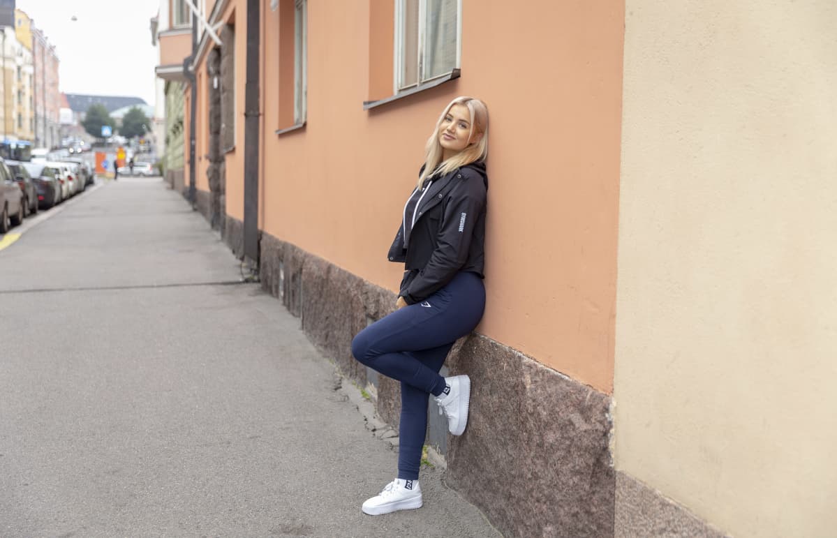 Sonja Aiello nojailee seinään Fredrikinkadulla Helsingissä, katsoo kameraan (kokokuva).