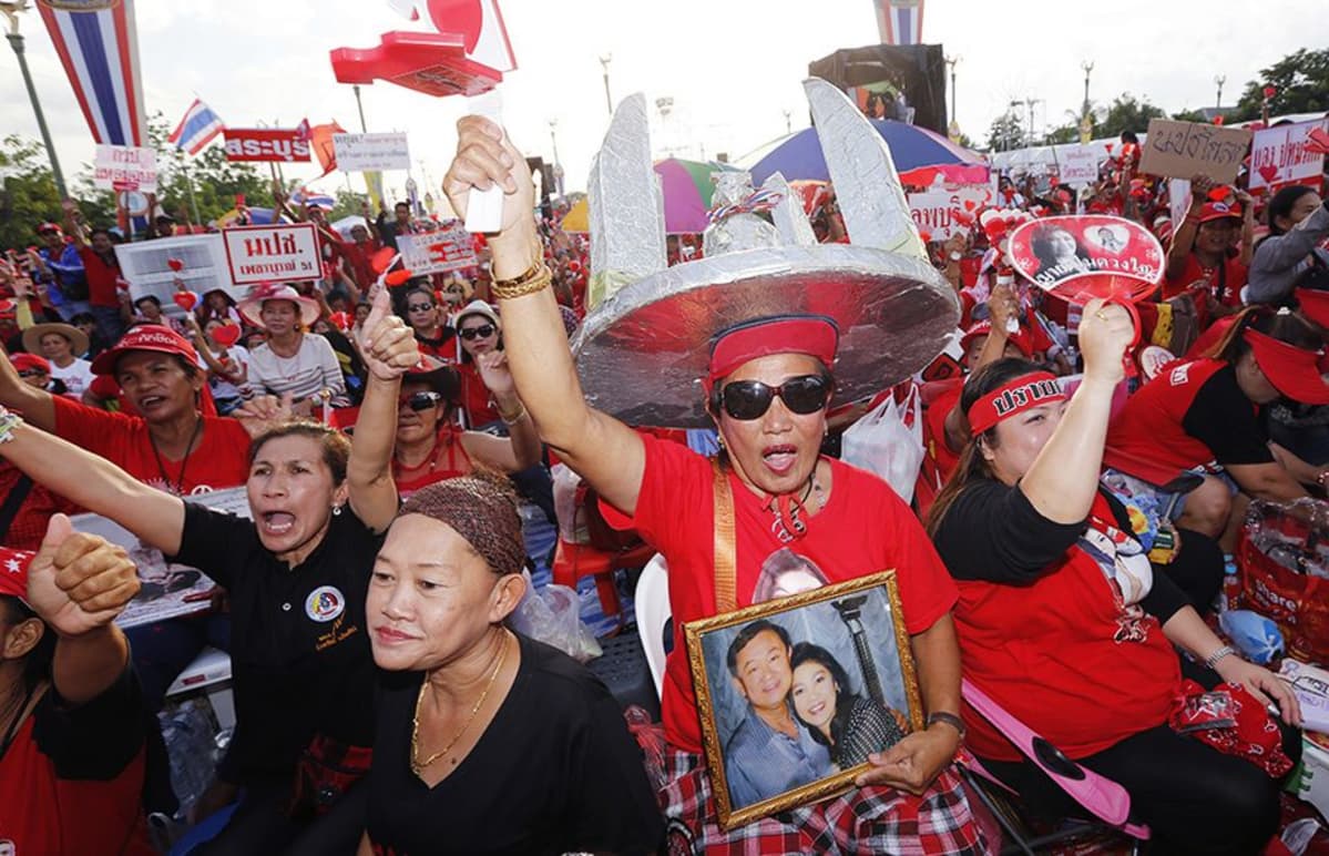 Mielenosoittajan pitelemässä valokuvassa näkyy Thaimaan syrjäytetty pääministeri Thaksin Shinawatra (vas.).