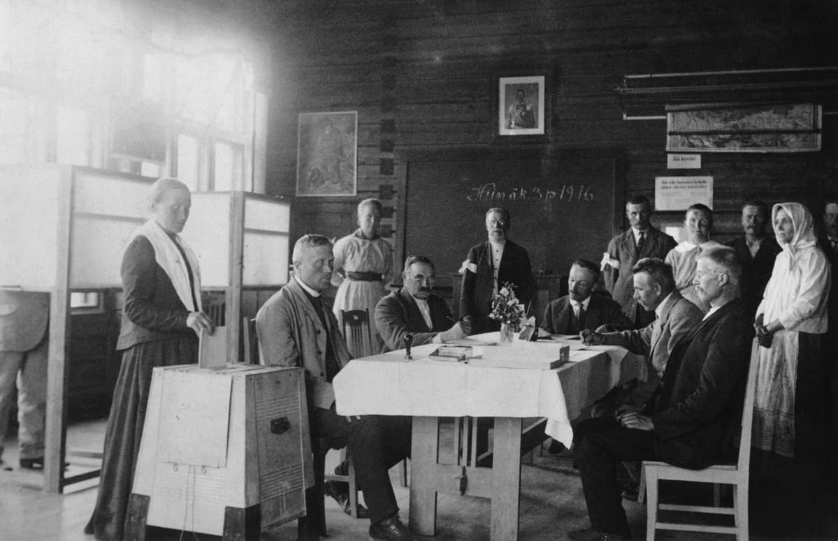 Vaalitoimitsijoita. Äänestäjä pudottaa äänestyslippuaan vaaliuurnaan Hauhon koululla eduskuntavaaleissa 1916.