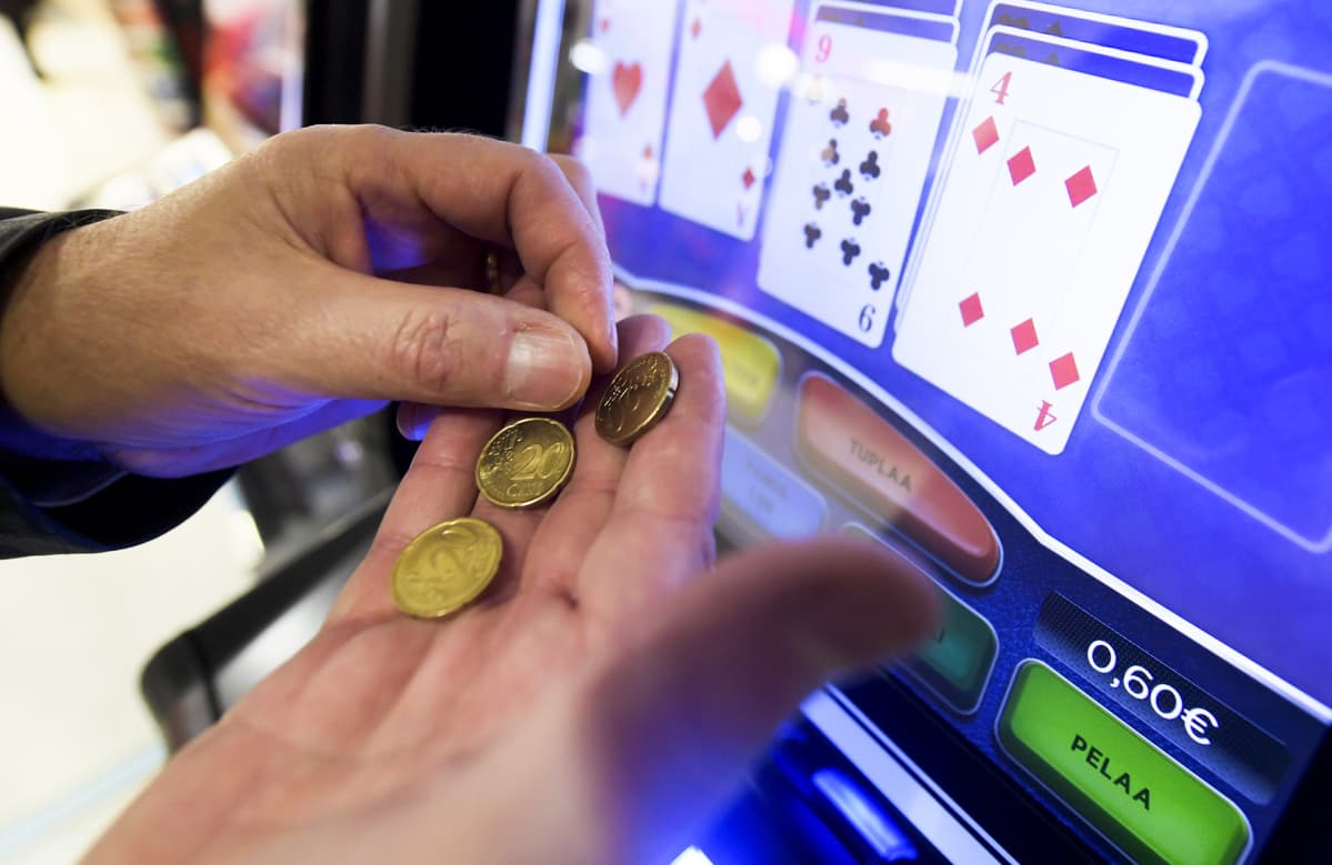 Miehne kämmenellä kahdenkymmenen sentin kolikoita ja taustalla näkyy peliautomaatti.