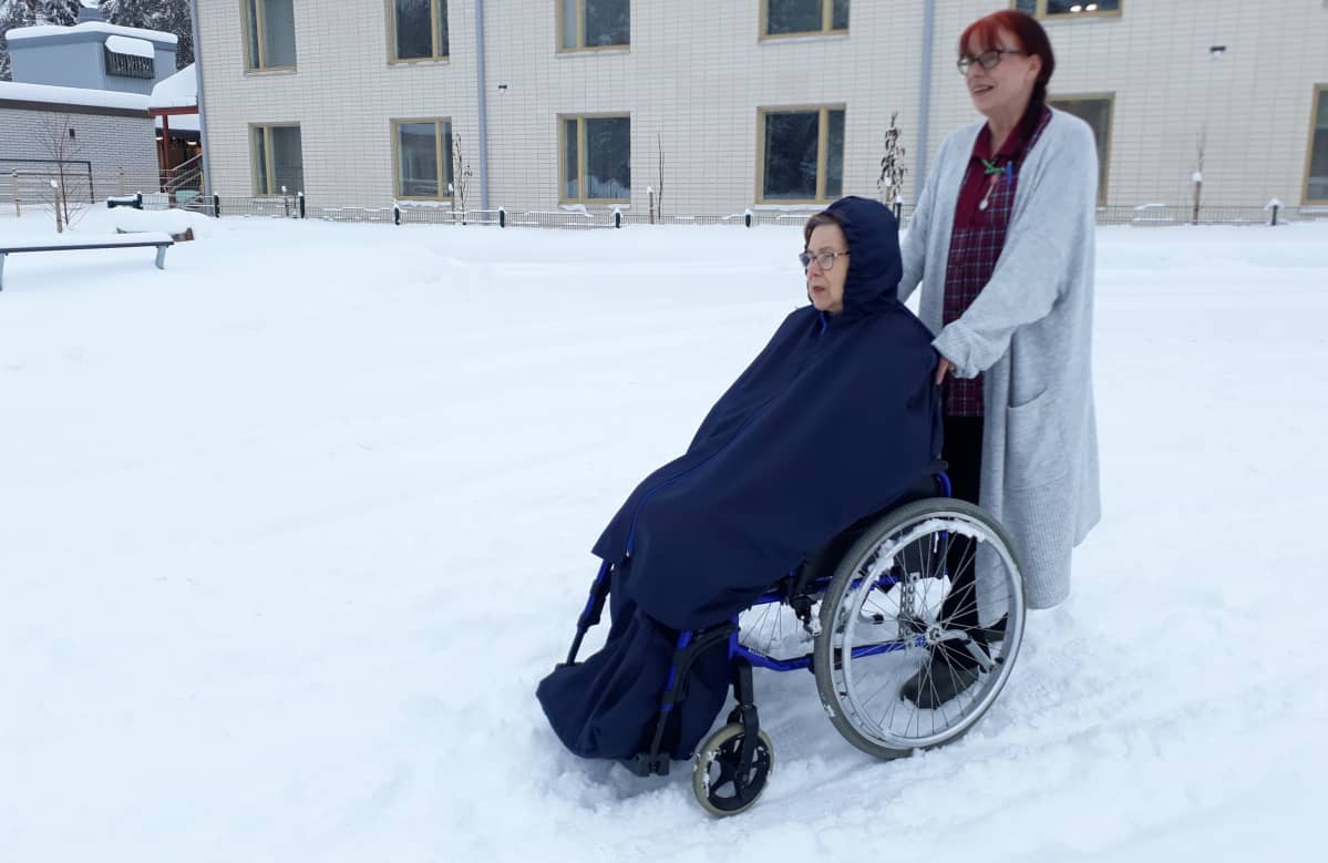 Hoitaja ulkoiluttaa pyörätuolissa istuvaa hoitokodin asukasta talvella.