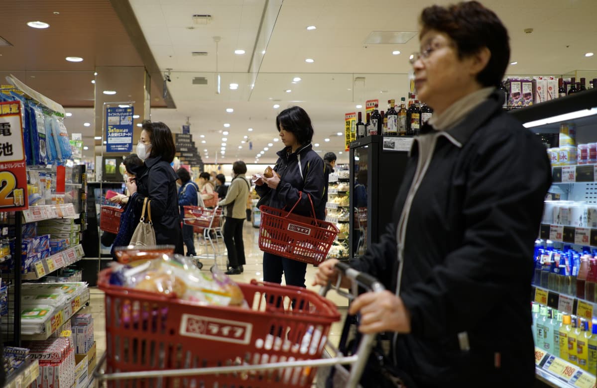 Japanilaisnaisia supermarketissa ostoskärryjen ja -korien kanssa.