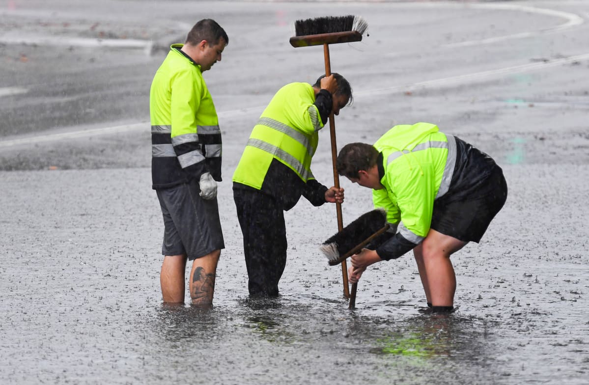 Kolme kunnan työntekijää yrittivät saada kaivoa vetämään harjanvarsilla. Vettä kadulla on puoleen pohkeeseen asti.