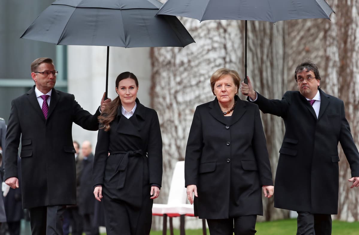 Sanna Marin ja Angela Merkel miesten pitelemien sateenvarjojen alla.