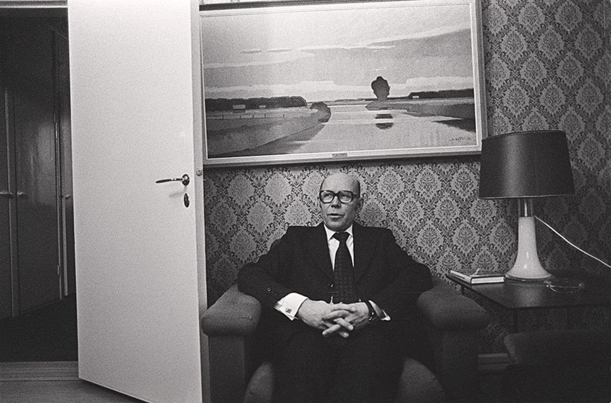 Keskustapuolueen kansanedustaja Eino Uusitalo istuu nojatuolissa kotonaan. Isokokoinen öljyvärimaalaus on hänen takanaan seinällä.