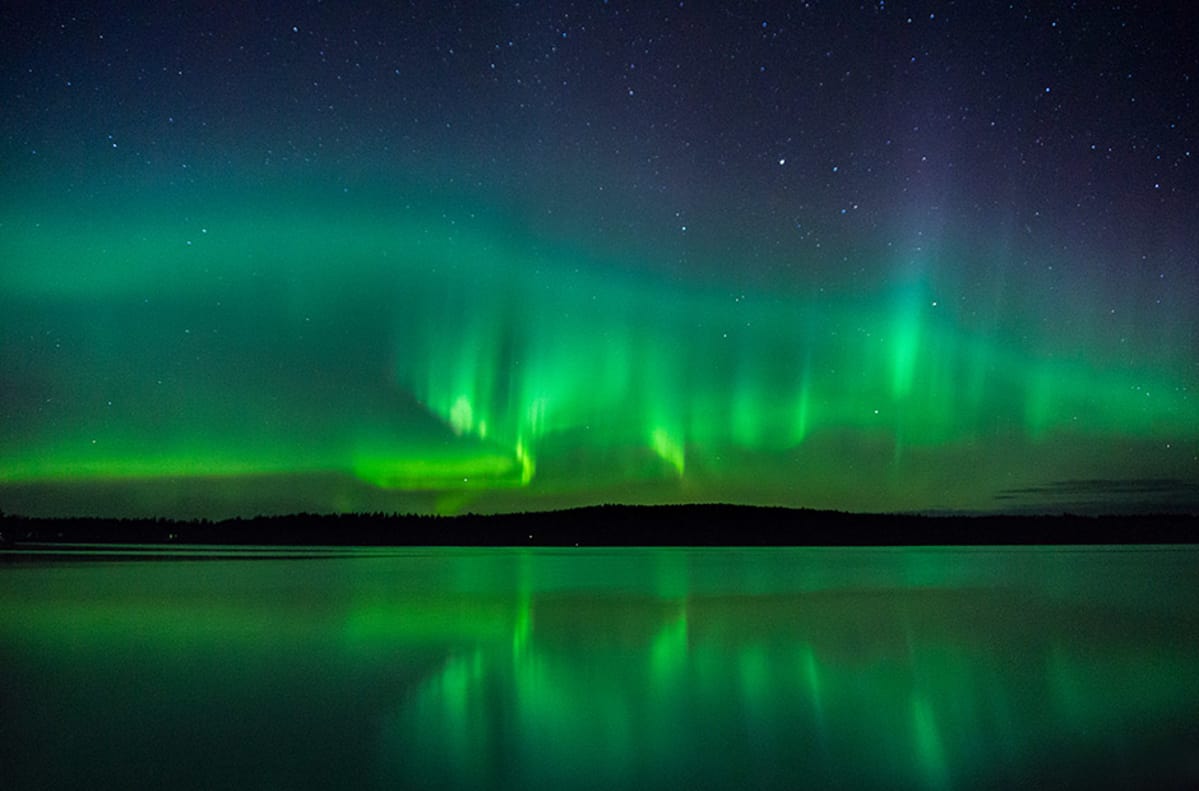Revontulet yötaivaalla järven rannalta nähtynä