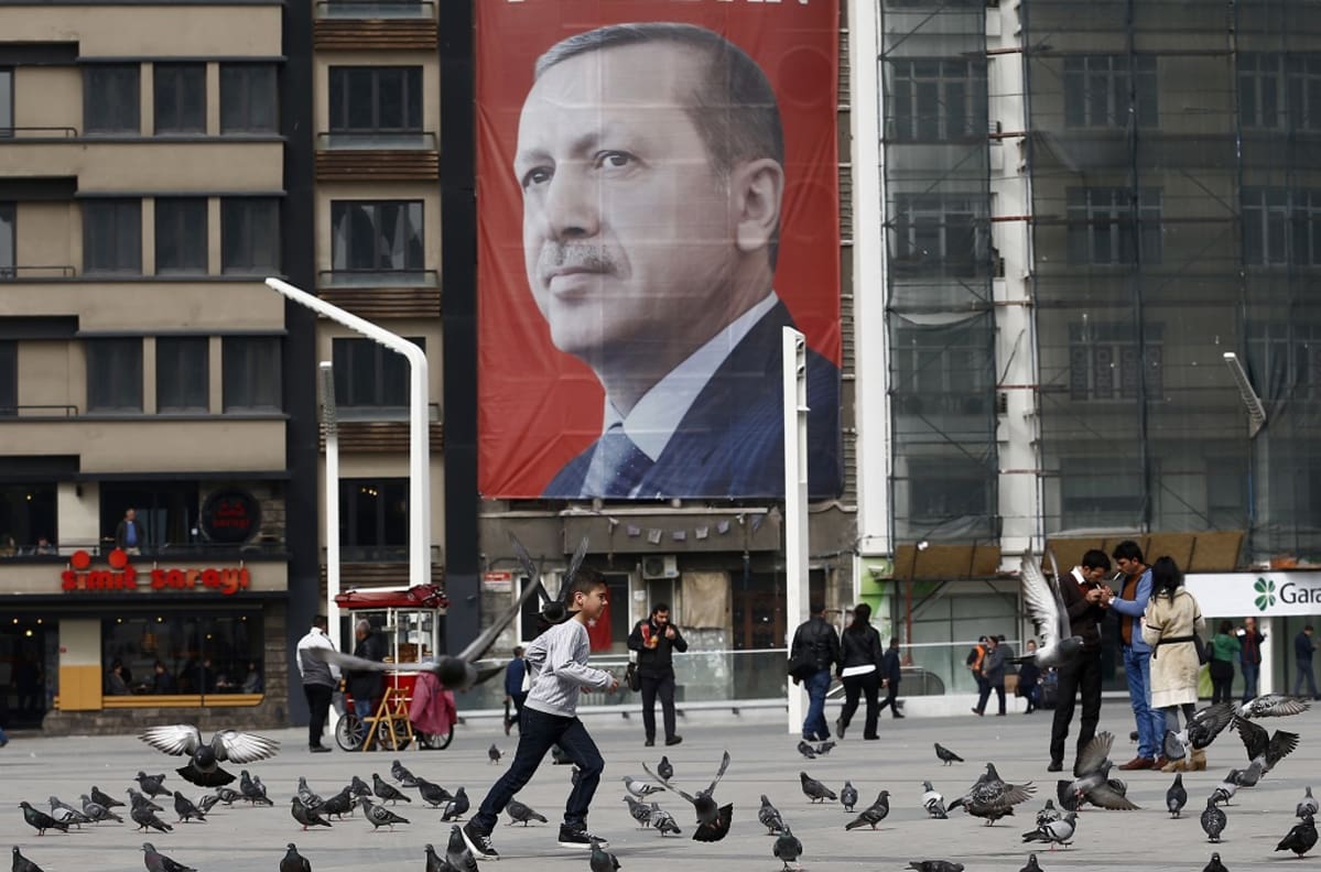 Recep Tayyip Erdoğanin jättimäinen kuva kerrostalon seinässä. Edustalla ihmisiä ja puluja.
