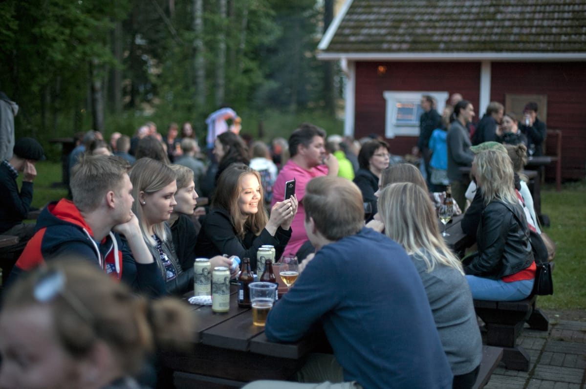 Paljon ihmisiä istumassa iltaa puisilla pitkillä penkeillä.