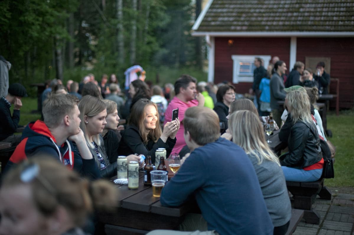 Paljon ihmisiä istumassa iltaa puisilla pitkillä penkeillä.