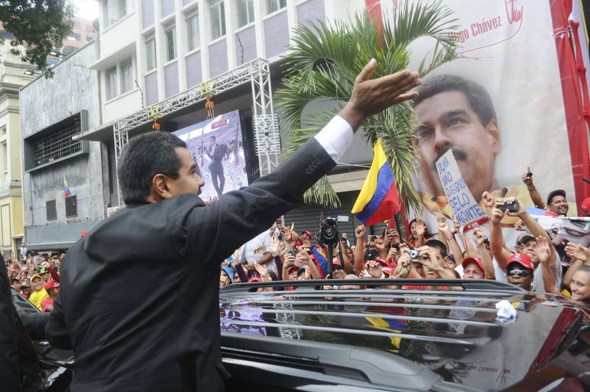 Tummaan pukuun pukeutunut presidentti Nicolas maduro tervehtii hänestä kuvia ottavaa ihmisjoukkoa.