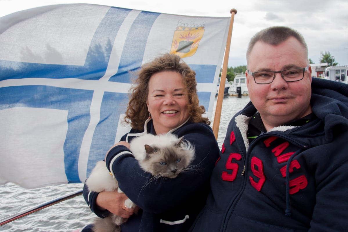 Päivi Kant-Bergroth ja Mikael Bergroth istuvat kissansa Jussin kanssa tuulisen veneen kannella.