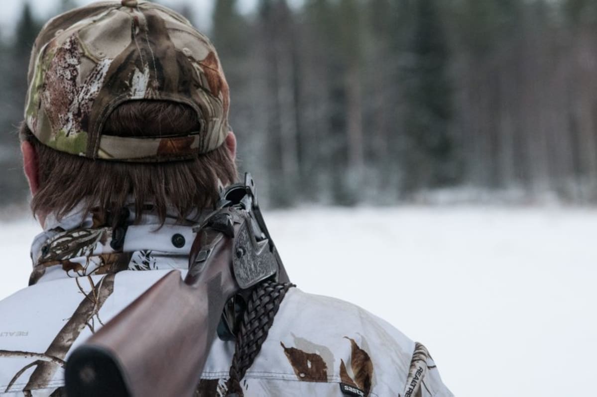 Metsästäjä takaapäin kuvattuna ase olalla.