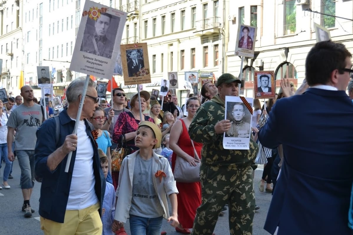 Arkiasuisia ihmisiä kantamassa julisteiksi tehtyjä valokuvia.
