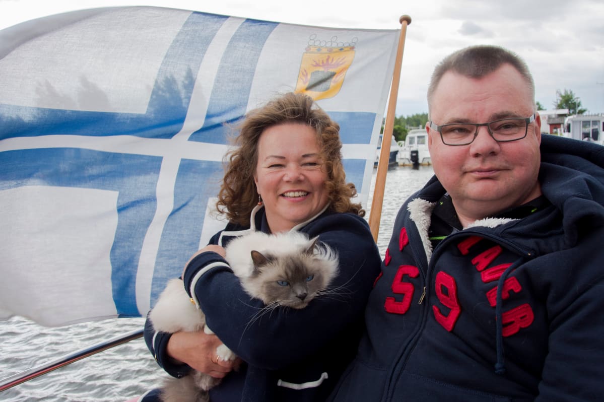 Päivi Kant-Bergroth ja Mikael Bergroth istuvat kissansa Jussin kanssa tuulisen veneen kannella.