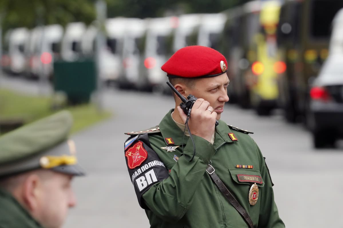 Sotilaspoliisi puhuu radiopuhelimeen. Taustalla ruumisautoja.