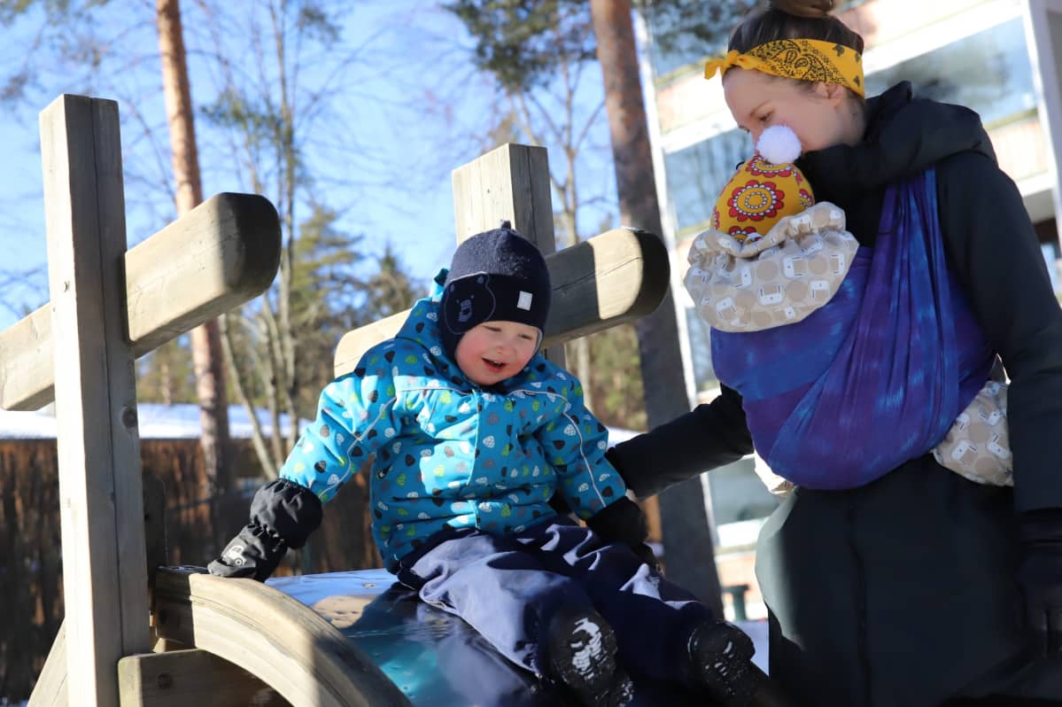 Pieni poika laskee liukumäkeä, äiti valvoo vieressä.