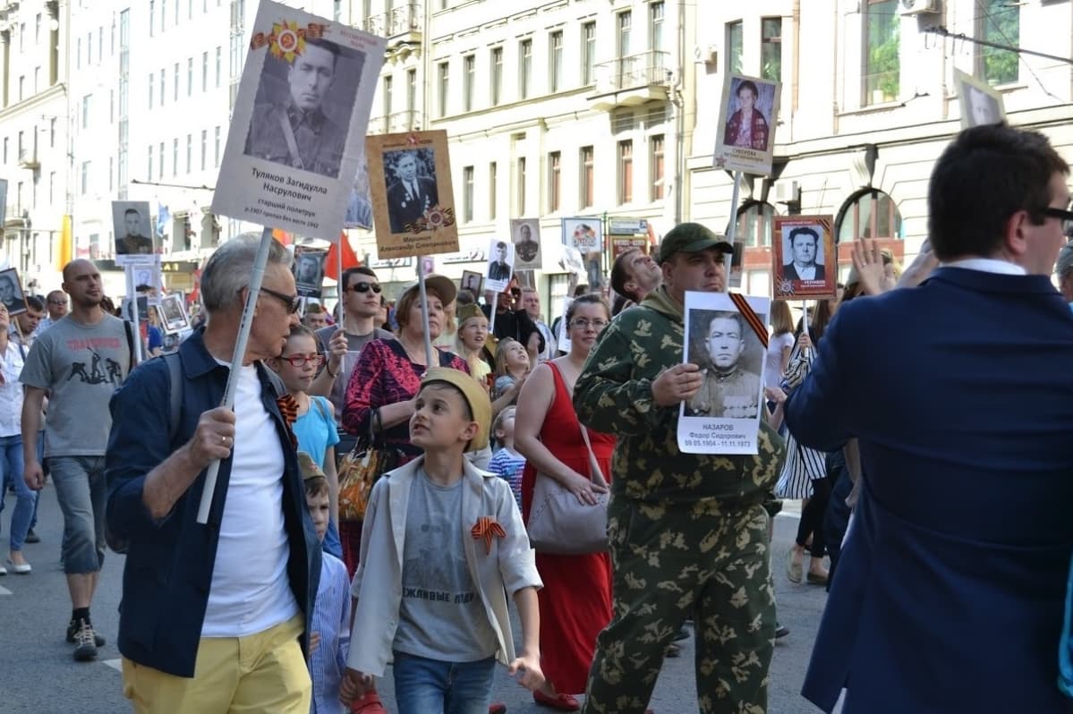 Arkiasuisia ihmisiä kantamassa julisteiksi tehtyjä valokuvia.