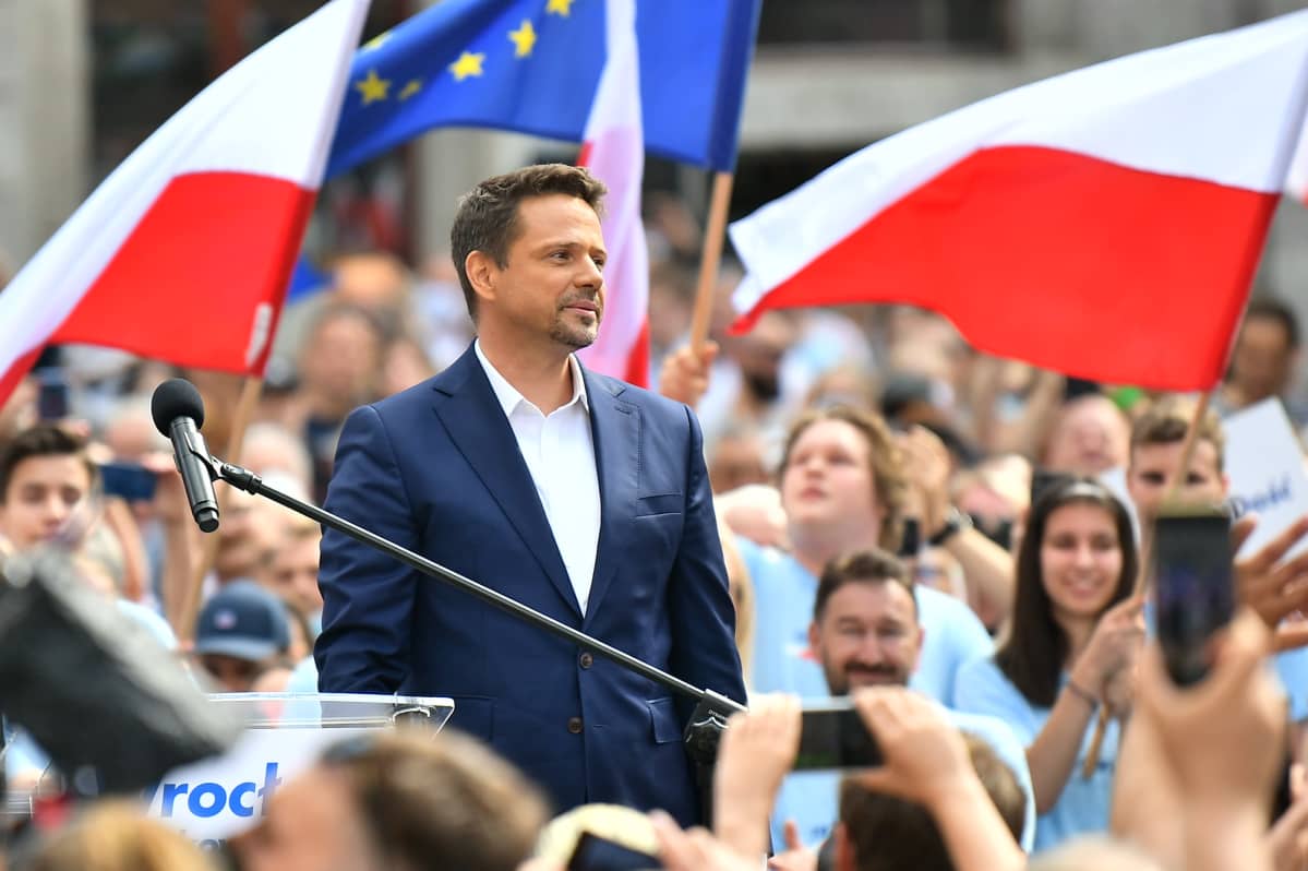 Trzaskowski kannattajiensa keskellä. Taustalla Puolan ja EU:n liput.