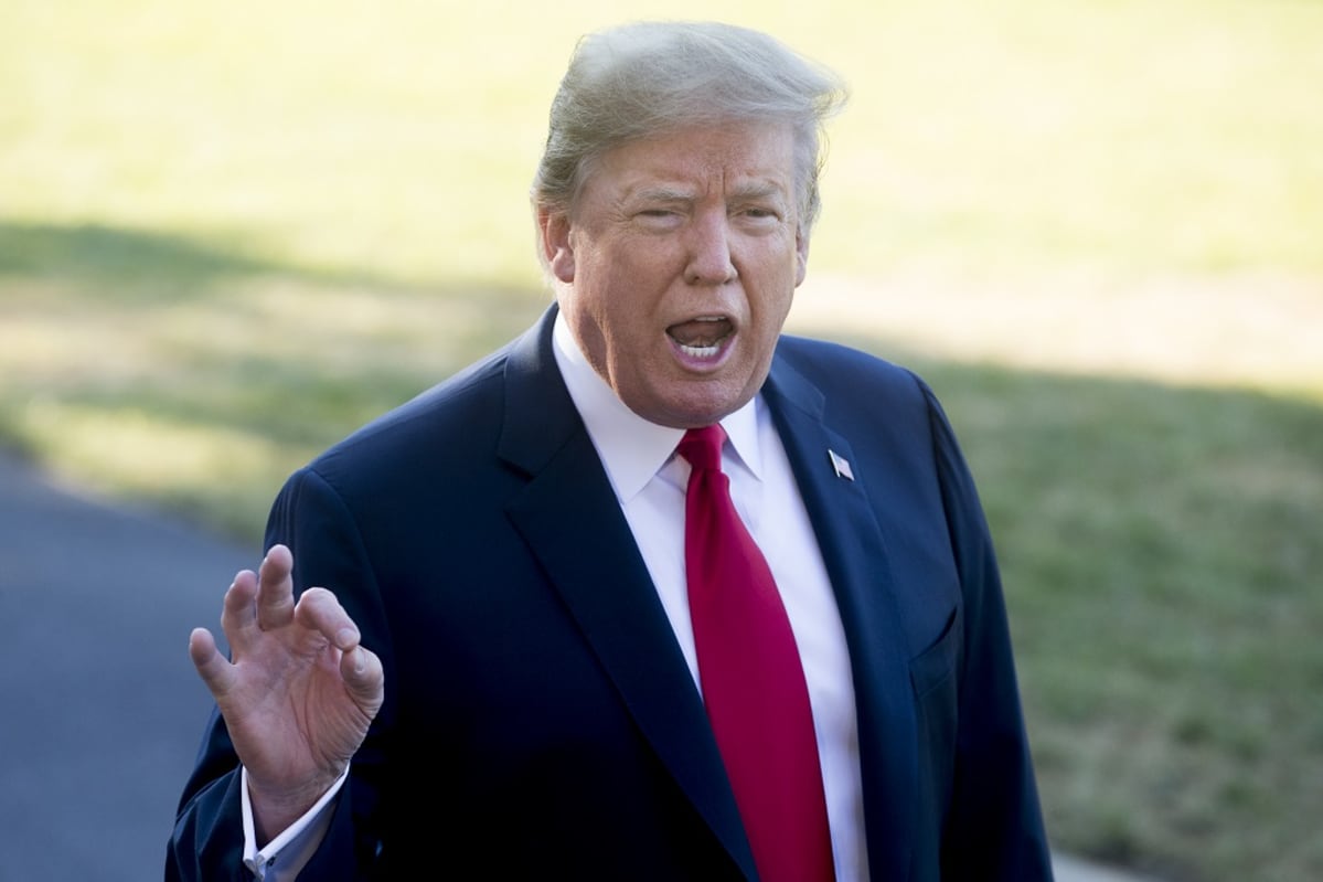 Trump puhuu Valkoisen talon pihamaalla. Hän elehtii oikealla kädellään pitäen etusormeaan ja peukaloaan yhdessä. Hänellä on tumma puku ja kirkkaanpunainen kravatti.