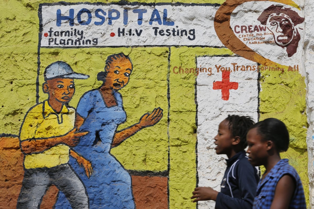 Naiset kävelevät ohi aids-neuvontaa mainostavan seinämaalauksen.