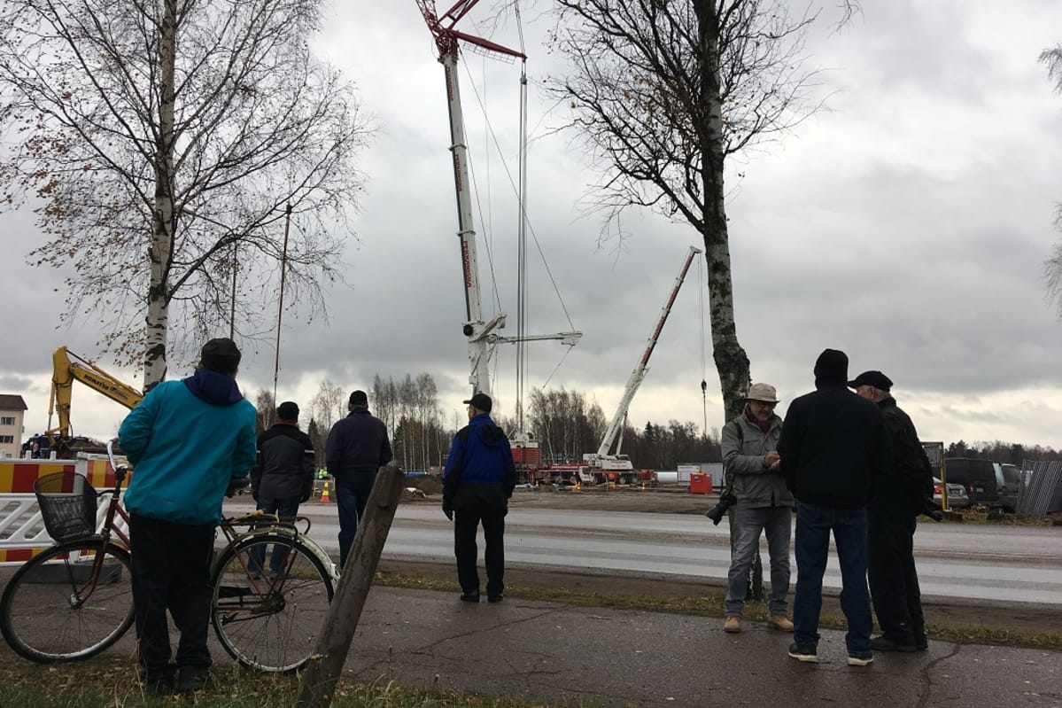 Ihmisiä katsomassa tien varressa satametrisen lipputangon nostoa pystyyn Haminassa.