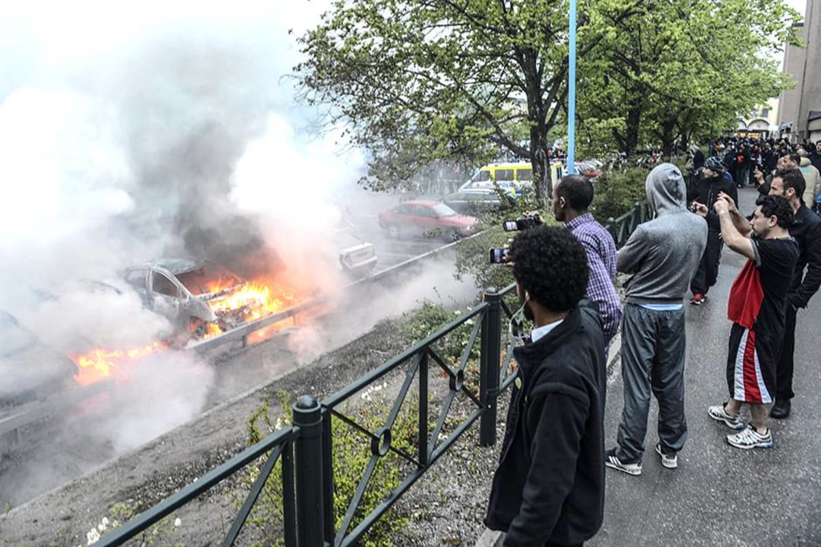 Ohikulkijat katsoivat mellakoitsijoiden sytyttämien autojen paloa Tukholman Rinkebyssä toukokuussa 2013.