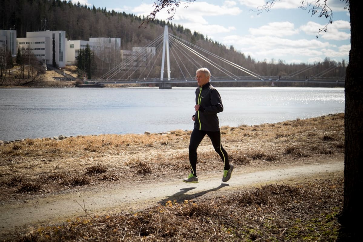Veryttelypukuinen Issakainen juoksee rantapolulla Jyväskylässä. Taustalla Mattilanniemen kävelysilta.