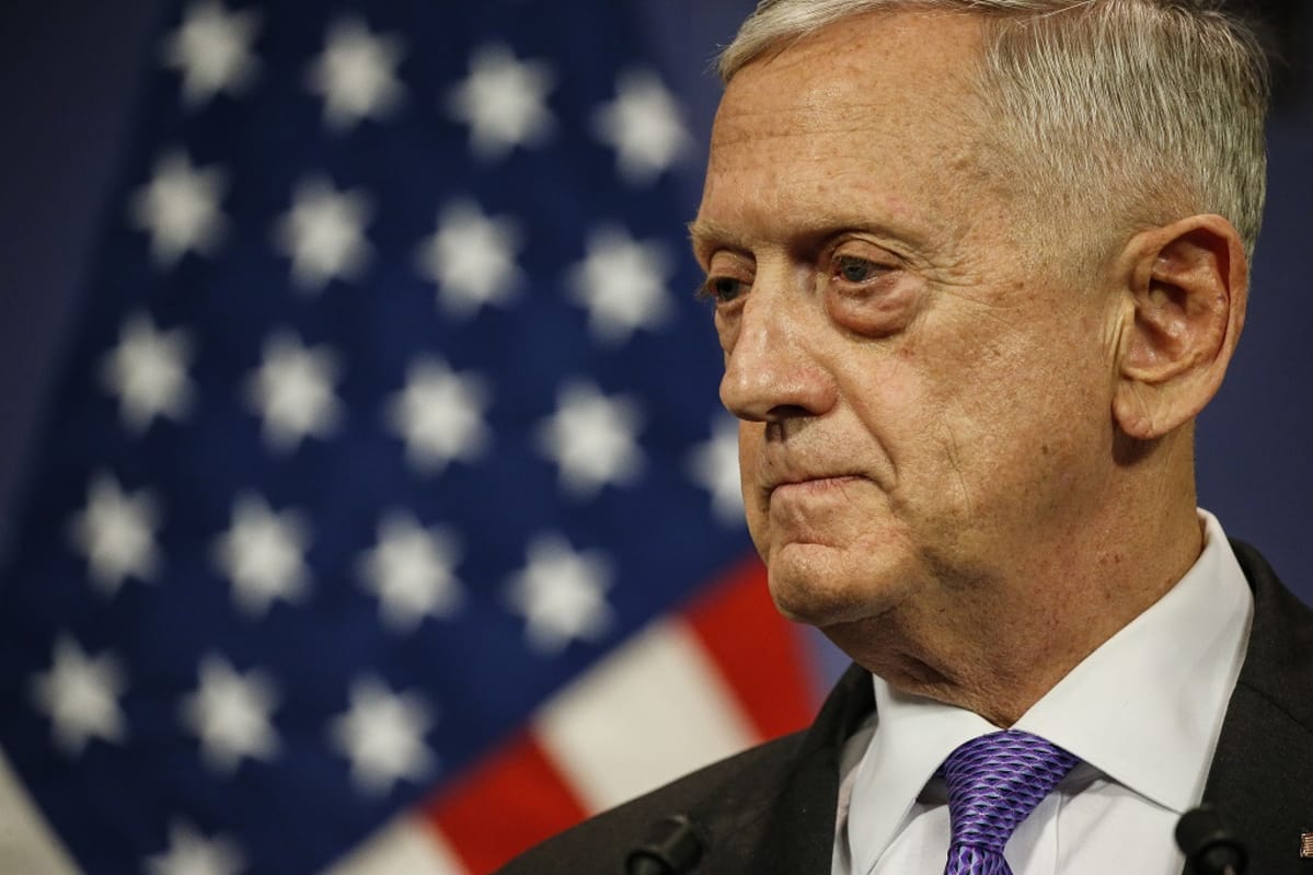 Jim Mattis tummassa puvussa, violetissa kravatissa, taustalla Yhdysvaltain lippu.