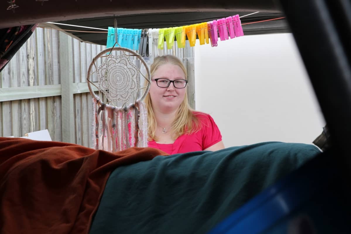 Kuvassa Emmi Vinberg kuvattuna pakettiauton takana. Auton takaosassa pyykkinaru, jossa pyykkipoikia.