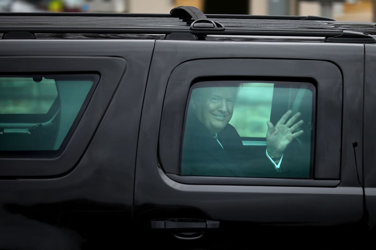 Trump vilkuttaa massiivisen mustan auton ikkunasta hymyillen leveästi.