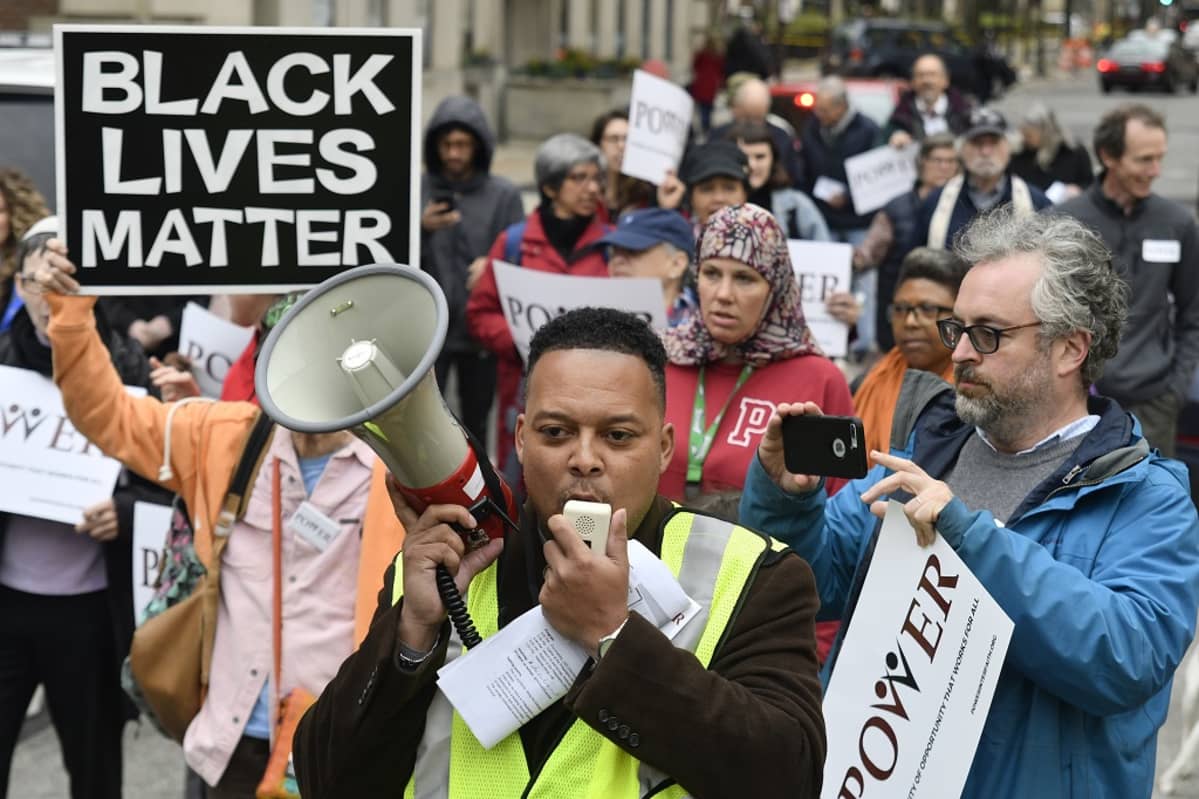 Kuvassa mielenosoittajia. Etualalla musta mies huutaa megafoniin. Taustalla kyltti, jossa lukee "Black lives matter".