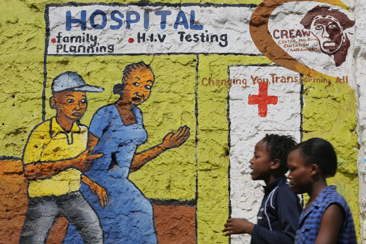 Naiset kävelevät ohi aids-neuvontaa mainostavan seinämaalauksen.
