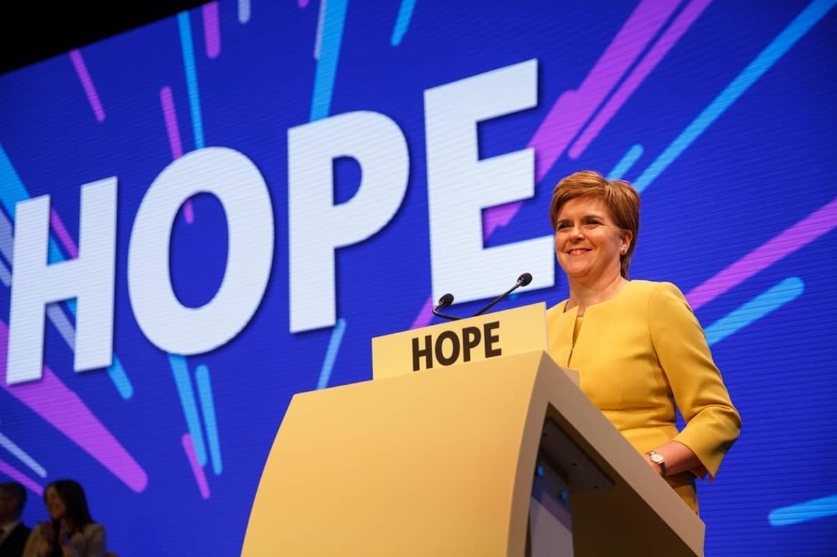 Kuvassa Skotlannin pääministeri Nicola Sturgeon lavalla puhujanpönton takana. Taustakankaalla lukee isoilla kirjaimilla teksti HOPE eli toivo.