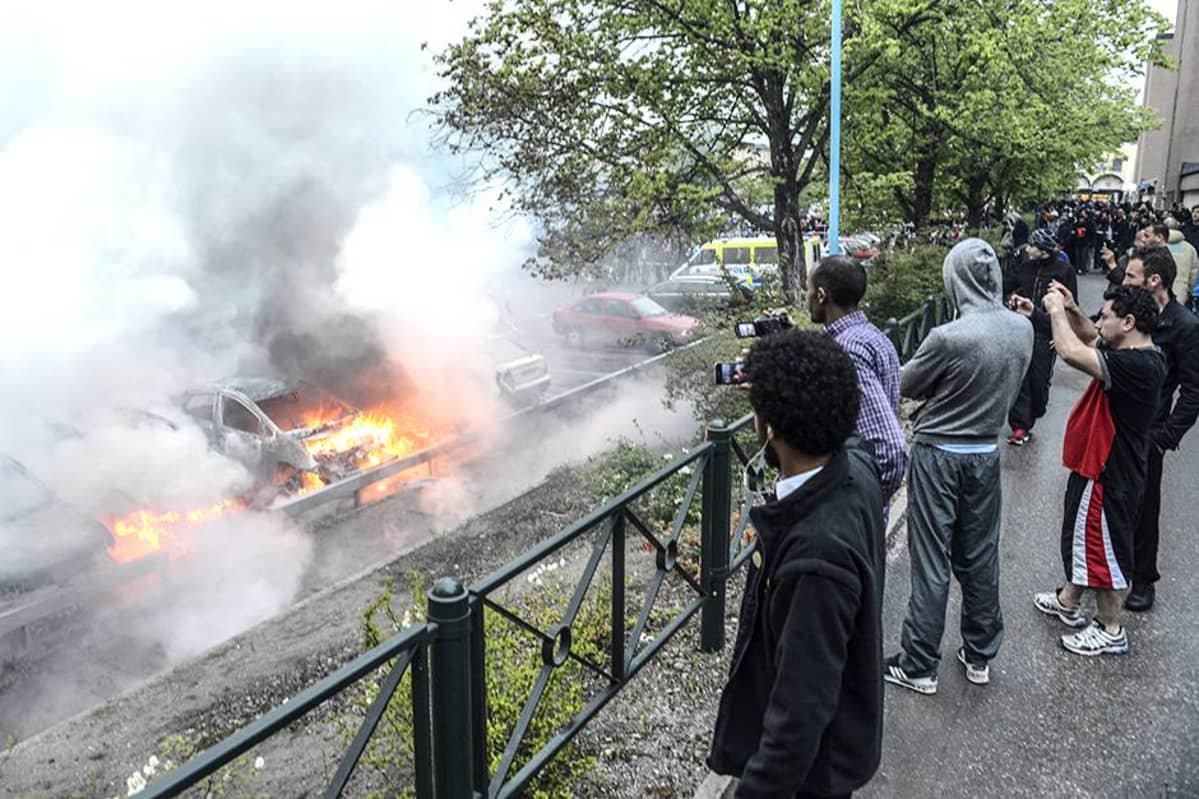 Ohikulkijat katsoivat mellakoitsijoiden sytyttämien autojen paloa Tukholman Rinkebyssä toukokuussa 2013.