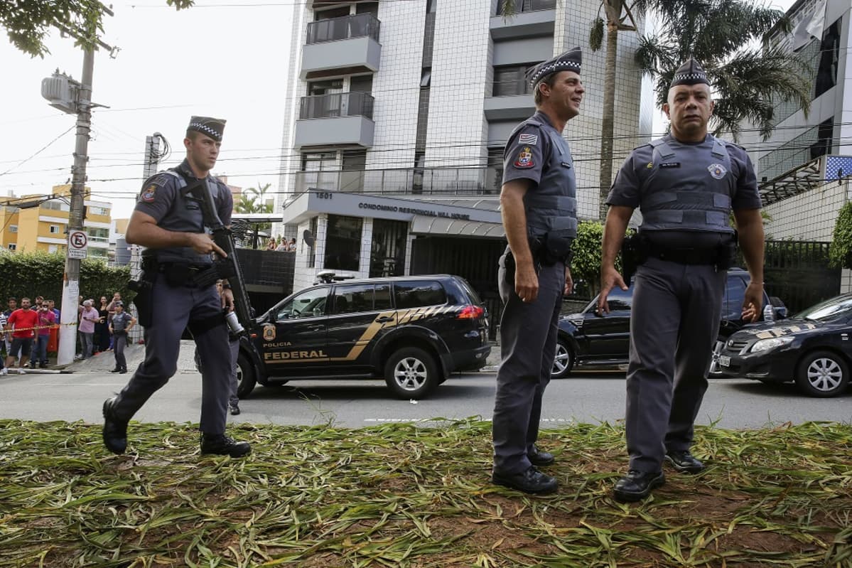 Kuvassa etualalla on kolme poliisia. Kaksi poliiseista seisoo kuvan oikeassa reunassa. Poliiseilla on yllään luotiliivit, päässään suikat. Univormut ovat sinervänharmaat. Kolmas poliisimies on tulossa vasemmalta, hänellä on kädessään jonkinlainen rynnäkkökivääri tai konepistooli. Taustalla näkyy kerrostalo, ja kadulla sen edessä on parkkeerattuna mustia poliisiautoja. Ainakin yhden auton kyljessä lukee sana 'federal'. Kuvan vasemmassa reunassa näkyy poliisin vetämän merkkinauhan takana tilannetta seuraavia kansalaisia.