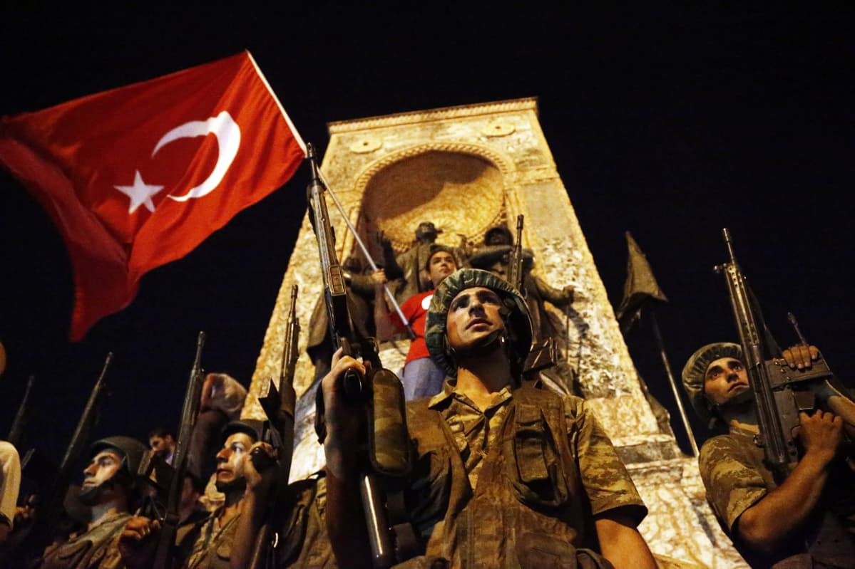 Turkkilaisia sotilaita ja Turkin lippua pitelevä mies Istanbulin Taksim-aukion keskellä olevan muistomerkin ympärillä.