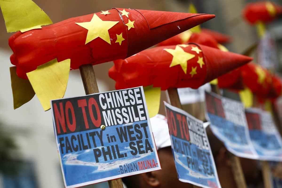 Mielenosoittajat pitelevät keppien päähän pulloista askarreltuja ohjuksia, jotka ovat Kiinan lipun puna-kelta-väreissä. Kyltissä lukee englanniksi: Ei Kiinan ohjusasemalle Länsi-Filippiinien merellä.