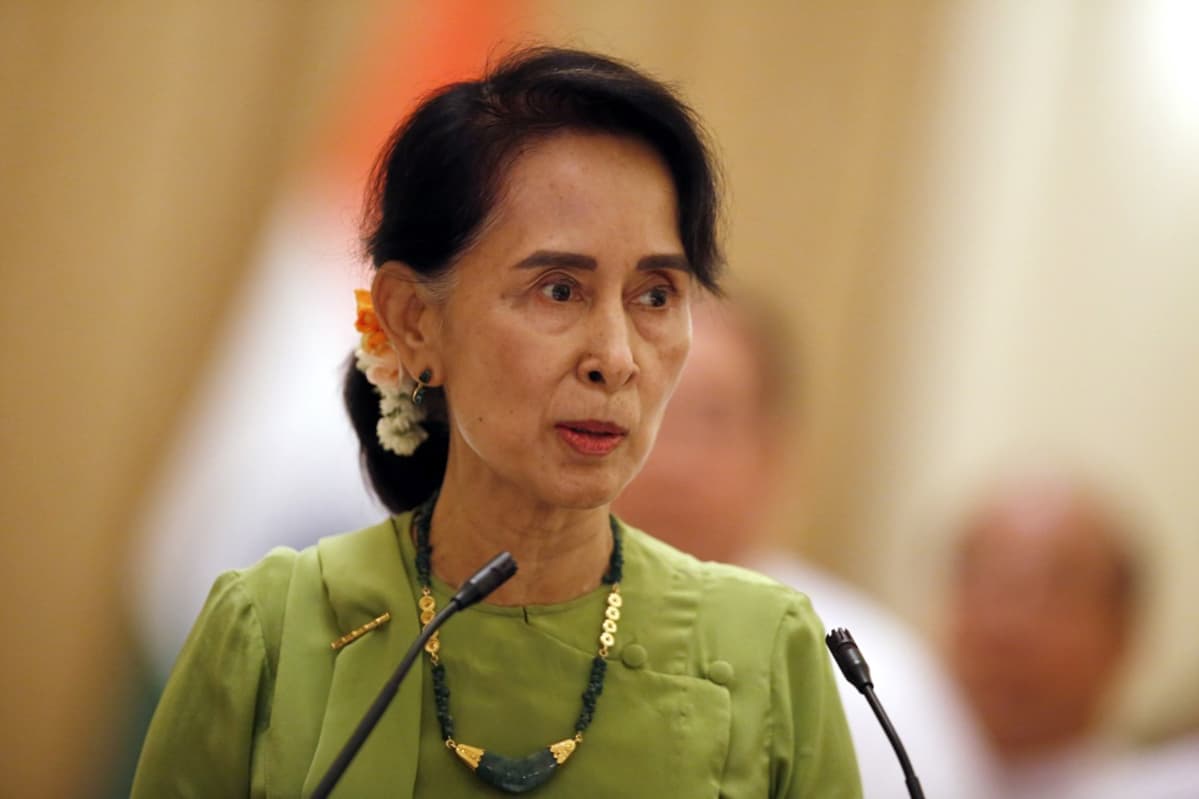 Aung San Suu Kyi vaaleanvihreässä asussa puhuu edessään oleviin mikrofoneihin.