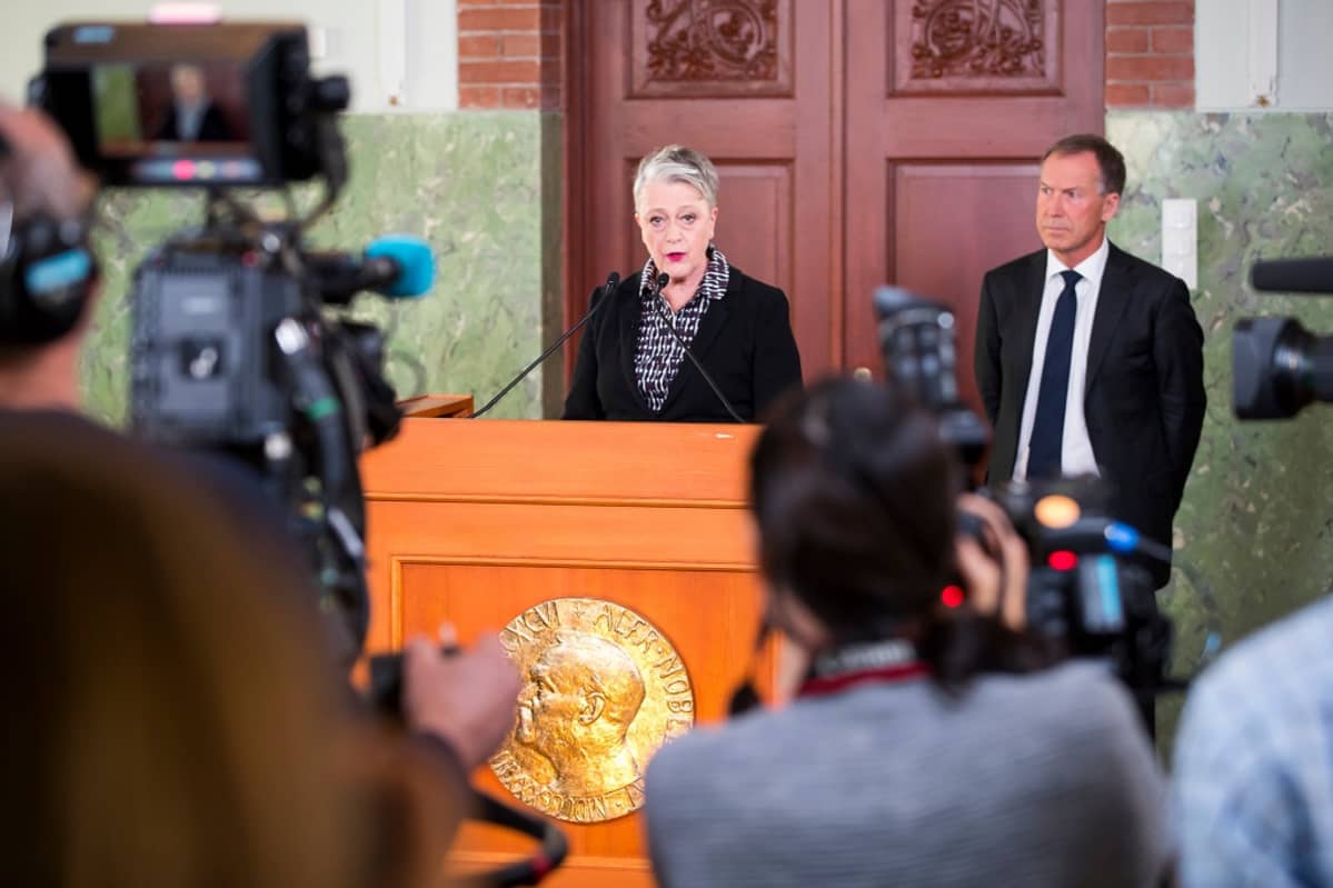 Nainen puhuu mikrofoniin toimittajien ympäröimänä.