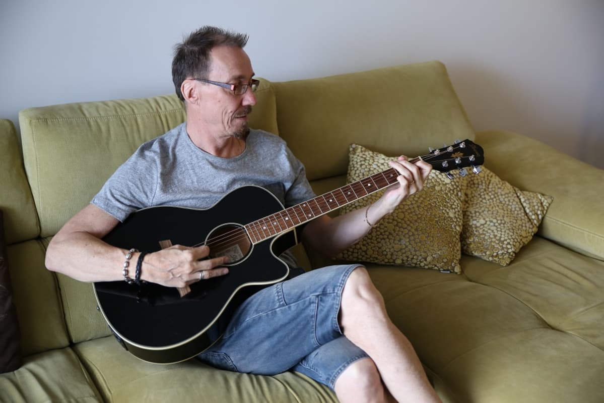 Kristian Olin istuu sohvalla ja soittaa akustista kitaraa.
