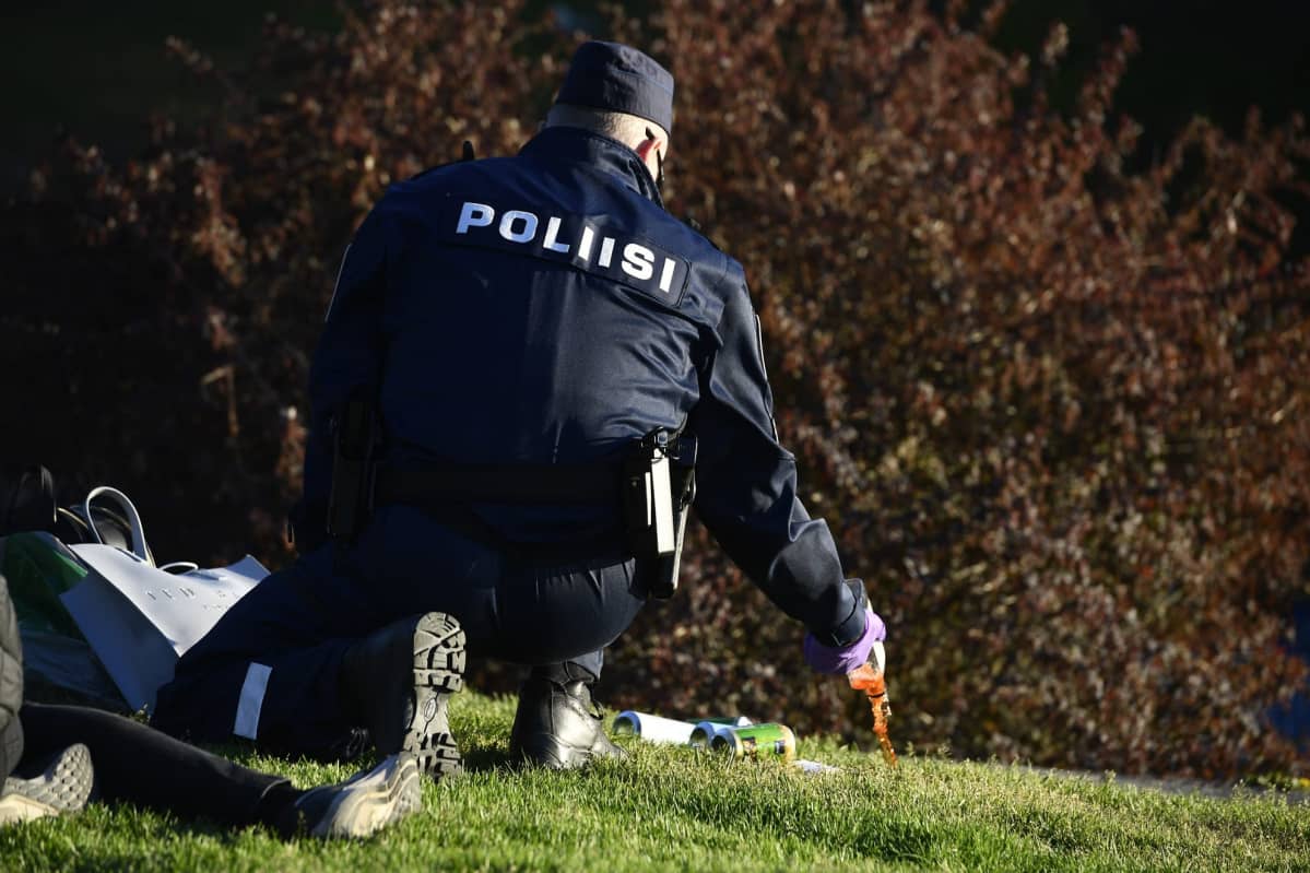 Poliisi kaataa alkoholia pullosta Hietaniemen uimarannalla kouluvuoden päätöksen juhlinnassa jota juhlittiin kauniissa auringonpaisteessa Helsingissä launatai-iltana.