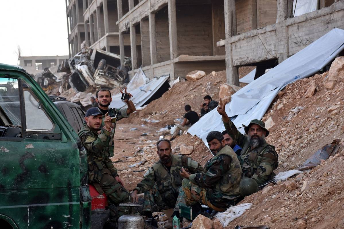 Syyrian armeijan istuvat tauolla ja näyttävät voitonmerkkiä Aleppon laitamilla. 