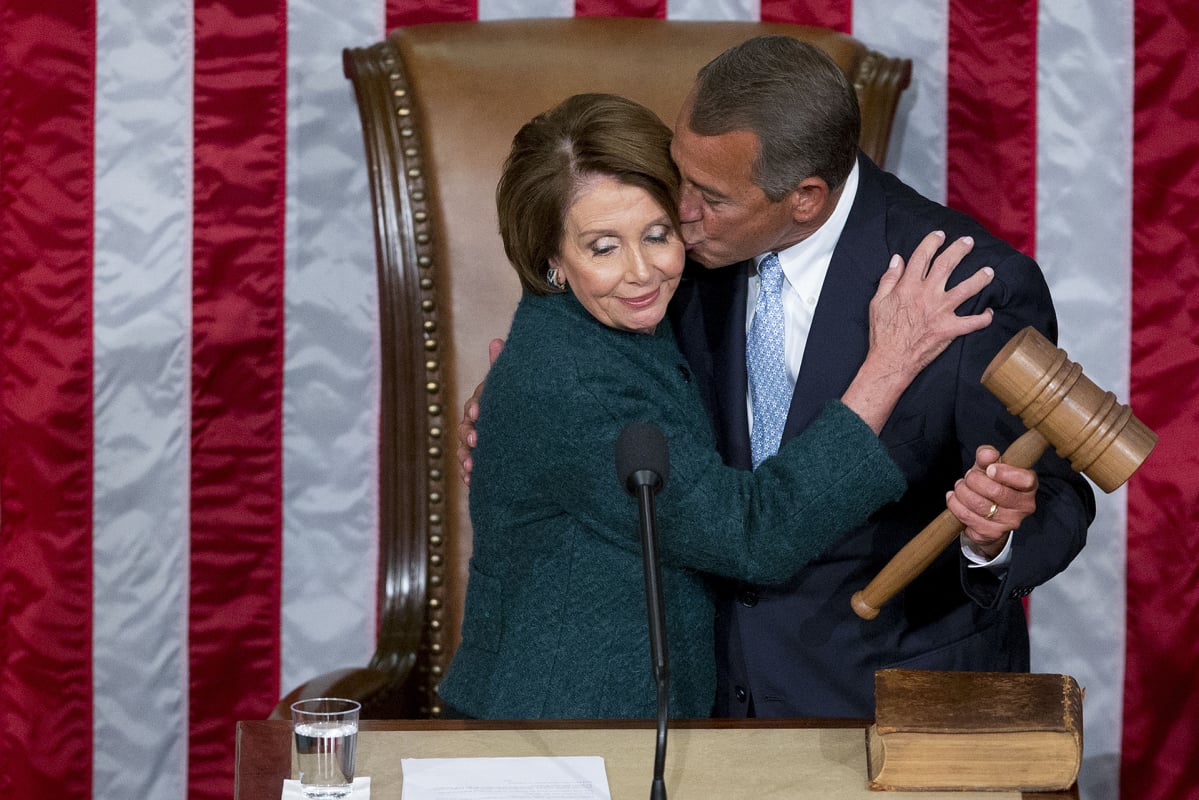 Republikaanipoliitikko John Boehner antaa Nancy Pelosille poskipusun. Taustalla Yhdysvaltain lippu.