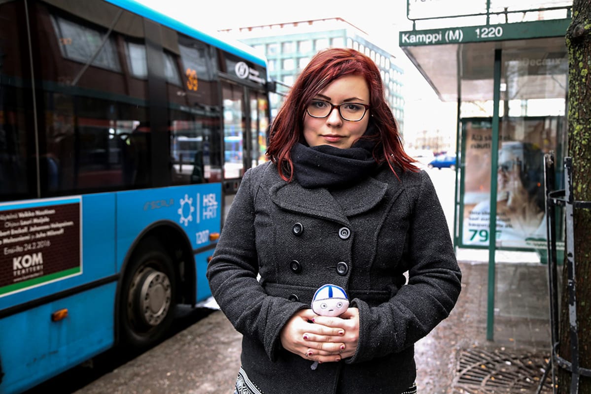 nainen busipysäkillä nukke kädessään