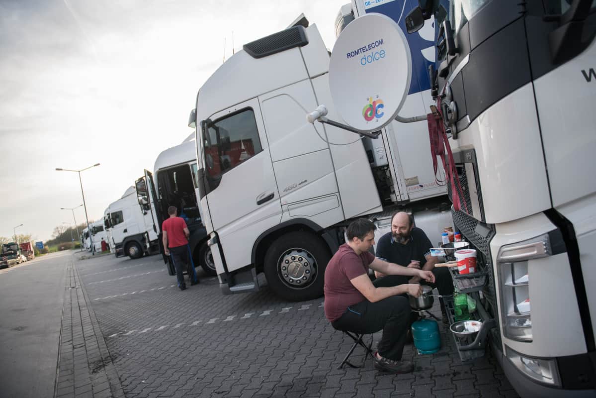 Kaksi miestä syö kuorma-autonsa edessä. Romanialaiset isä ja poika Ionel ja Daniel Lazar laittavat itse ruokaa tien päällä aina, kun voivat.