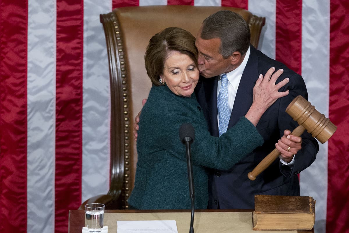 Republikaanipoliitikko John Boehner antaa Nancy Pelosille poskipusun. Taustalla Yhdysvaltain lippu.