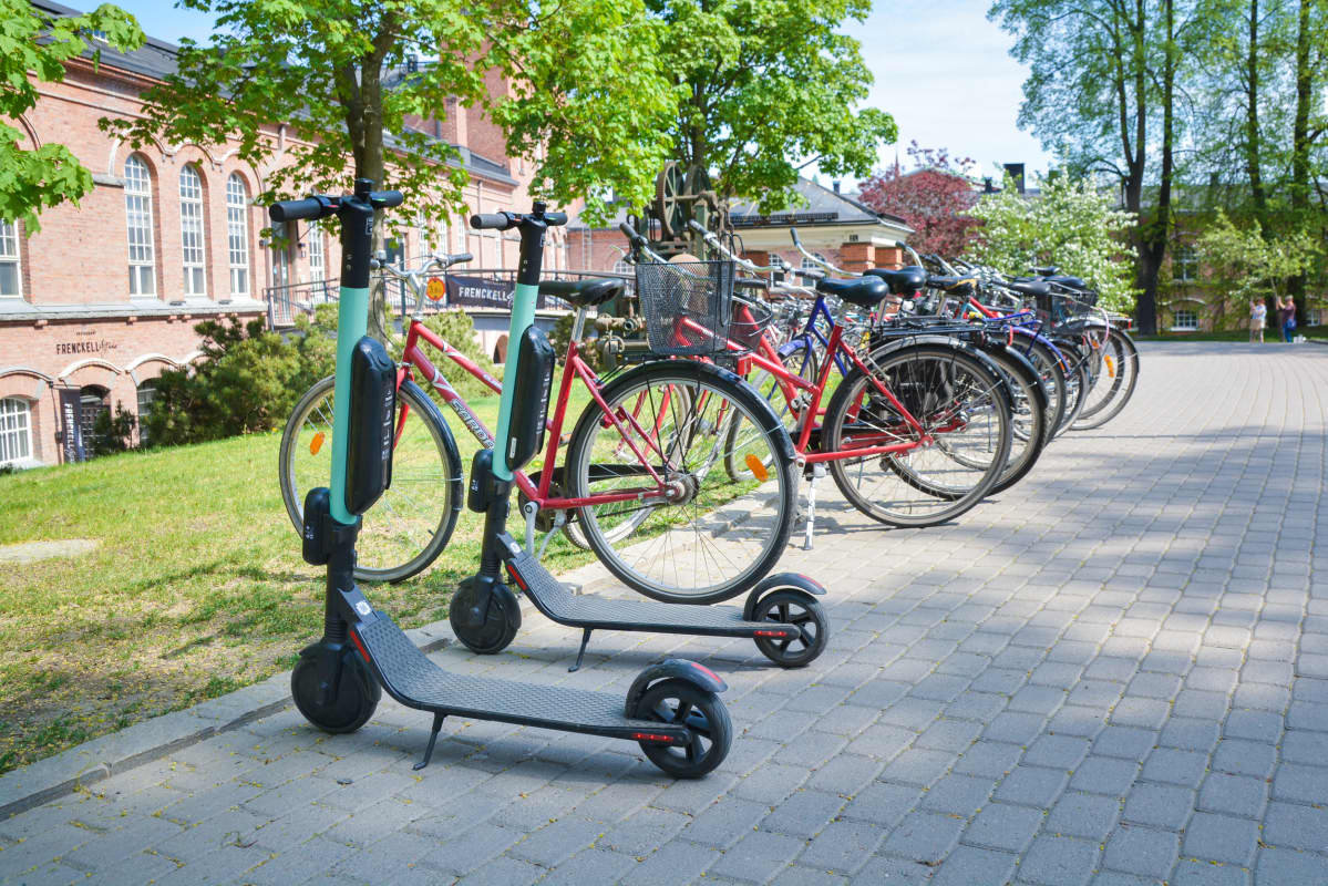 Kaksi sähköpotkulautaa pysäköitynä pyörärivin jatkoksi kevyen liikenteen laidalla.