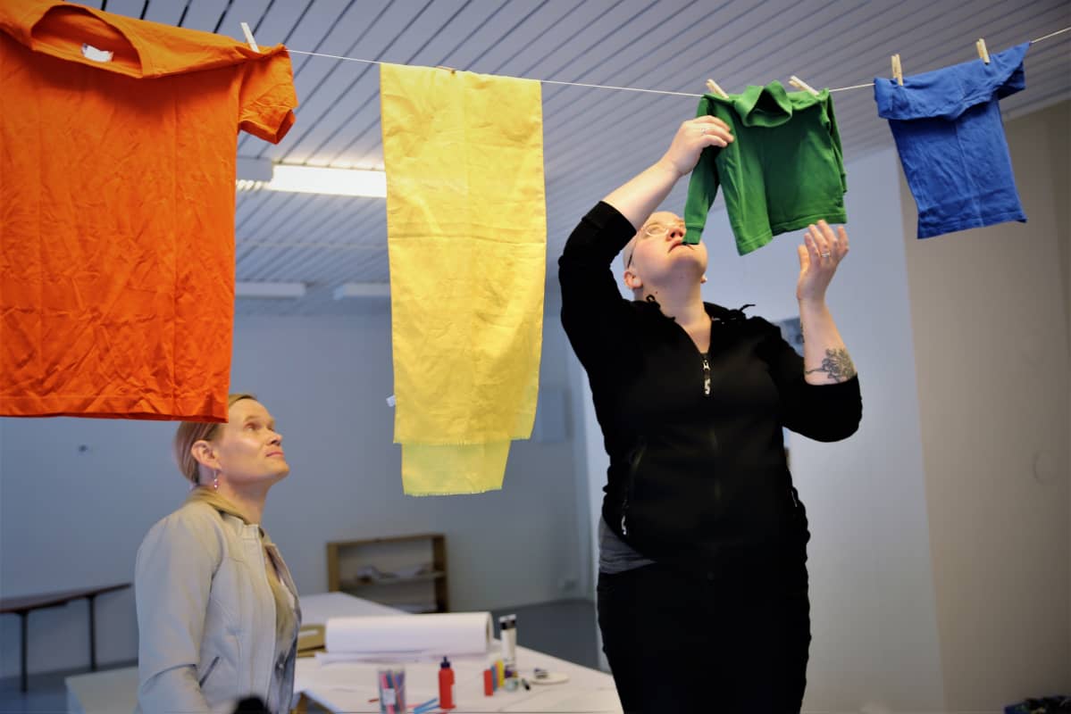Saana Lind ja Aurora Känsäkangas ripustavat värijärjestyksessä vaatteita sisällä olevalle pyykkinarulle Pride-viikon kunniaksi.