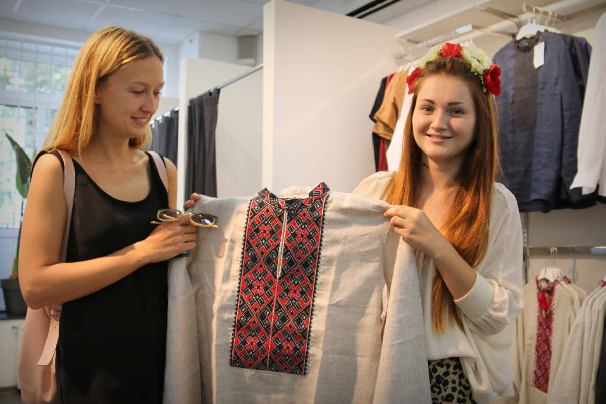 Ostoksilla olevat tytöt esittelevät kameralle vyšyvanka-paitaa vaatekaupassa.
